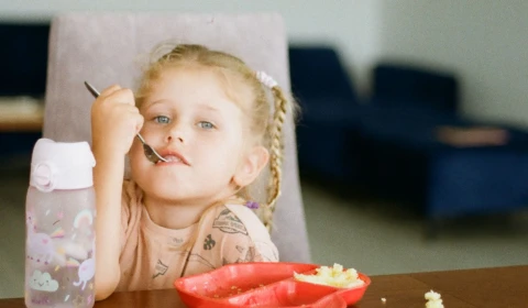 Photograph of a young girl sitting at a table, eating