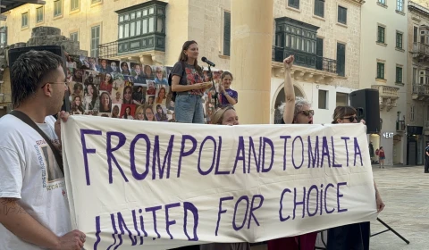 A group of people in a street hold a banner reading