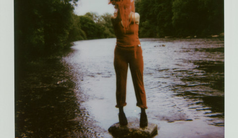 Person standing on a stone in the middle of a lake with a splash of paint over their face