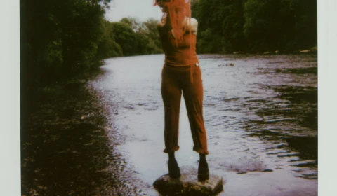 Person standing on a stone in the middle of a lake with a splash of paint over their face