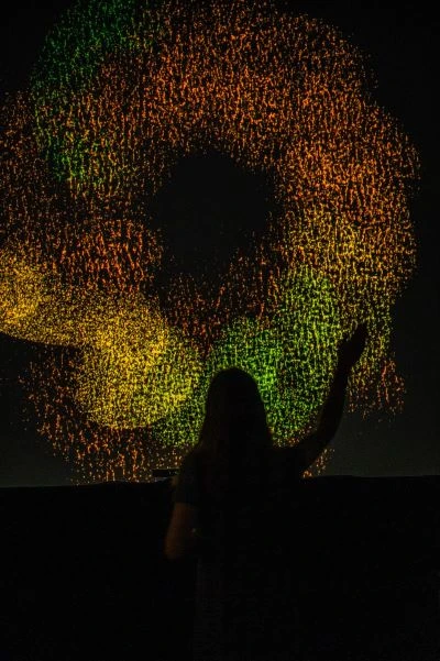 Swirling doughnut shape made up of many dots, in green, orange and yellow