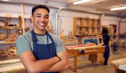 Man smiling with arms folded stood in a woodwork workshop