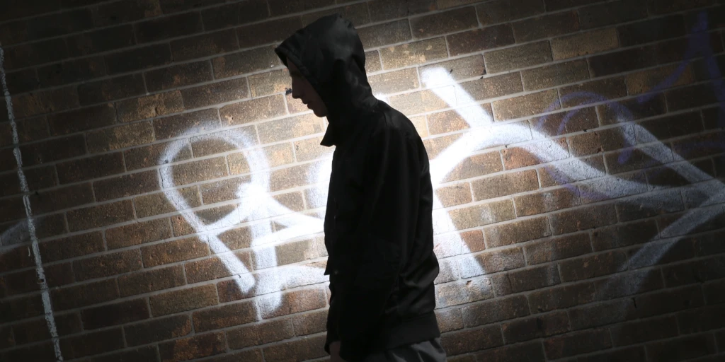 Photograph of the shadow of a young person in front of a wall with graffiti on it.