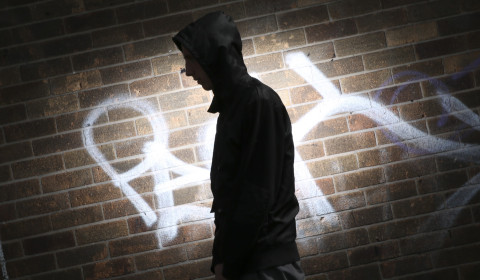 Photograph of the shadow of a young person in front of a wall with graffiti on it.