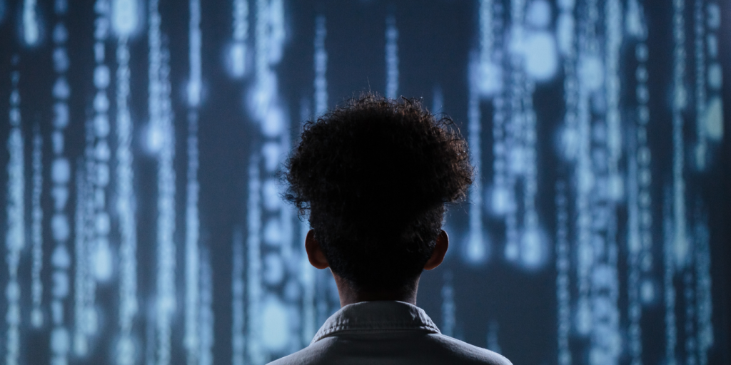 Silhouette of the back of someone's head who is standing in front of a screen with futuristic IT images on it