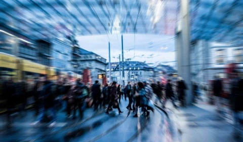 A blurred city scene shows crowds crossing tram tracks, capturing the fast pace and energy of urban life.